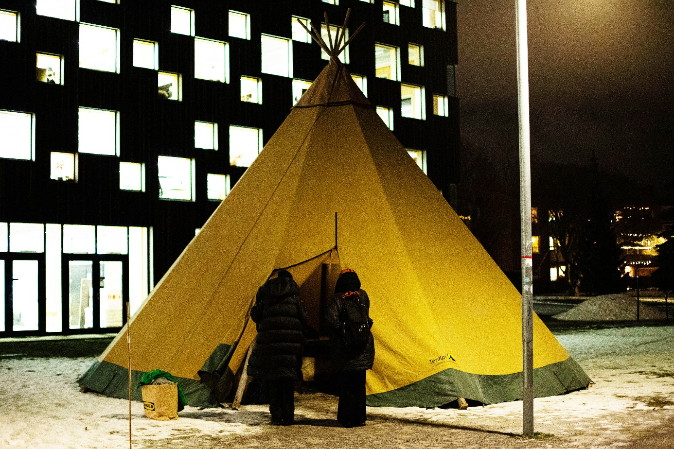 People entering a yellow tentipi situated on snowy ground at the Arts Campus of Umeå University, Sápmi/Sweden