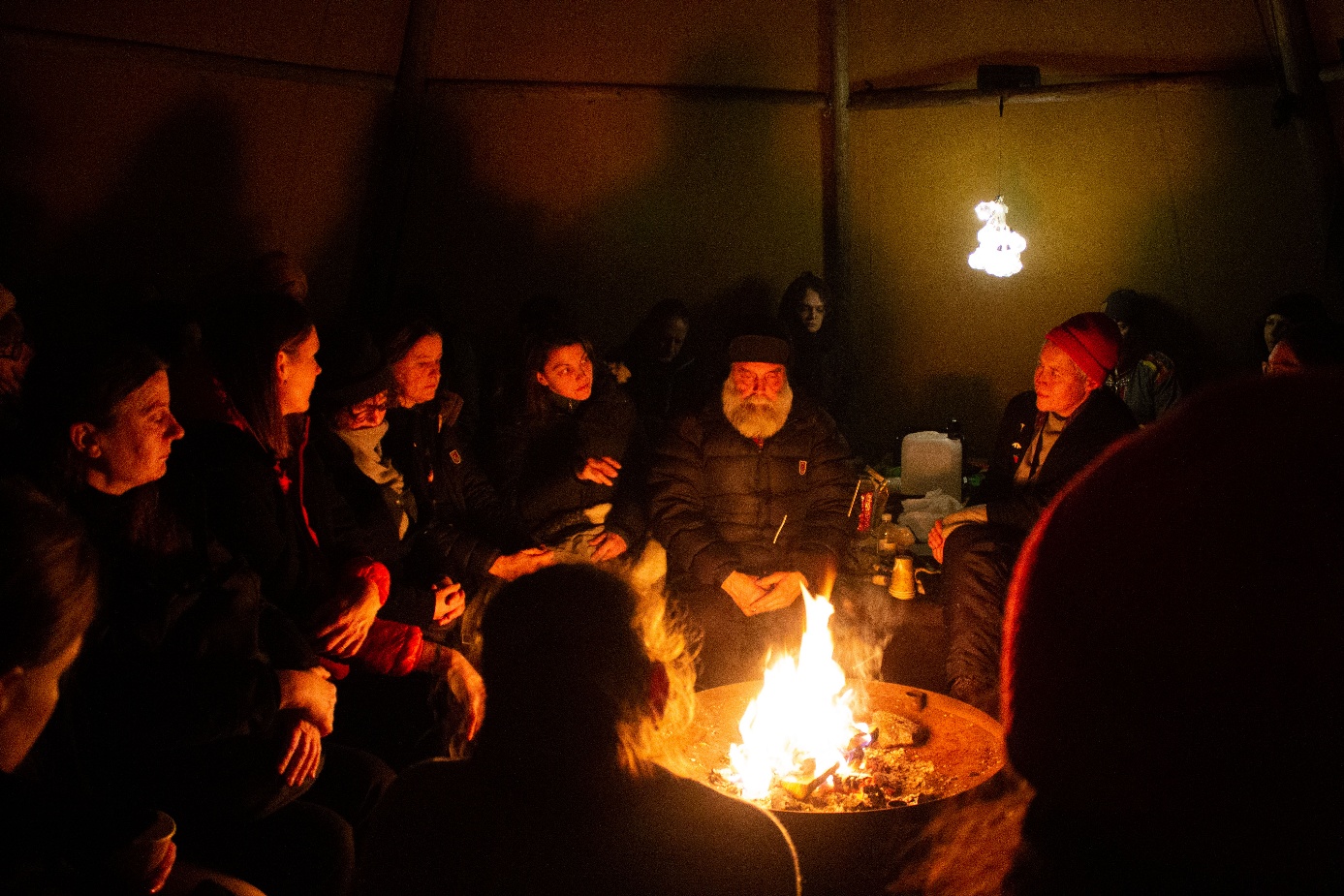 People gathering around a fire in the darkness of a tentipi