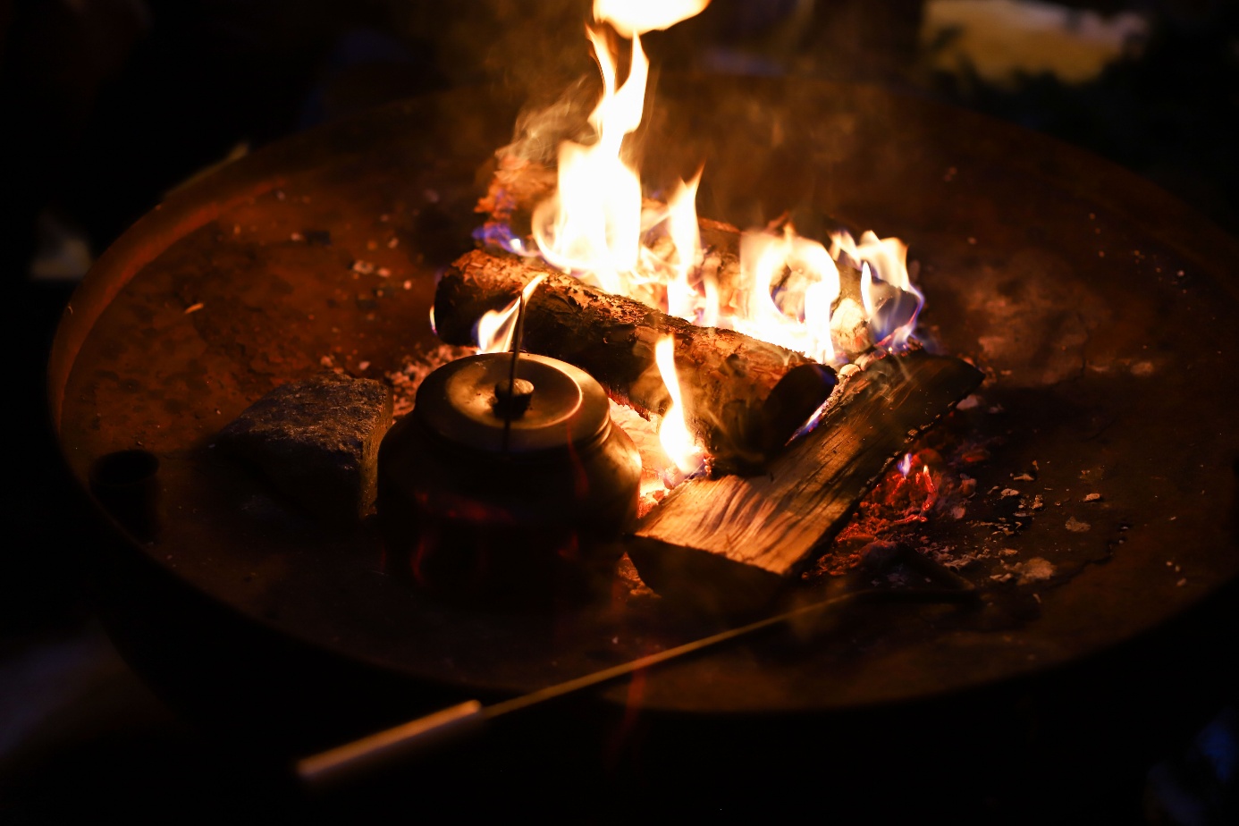 Open fire with a coffee pot next to burning logs
